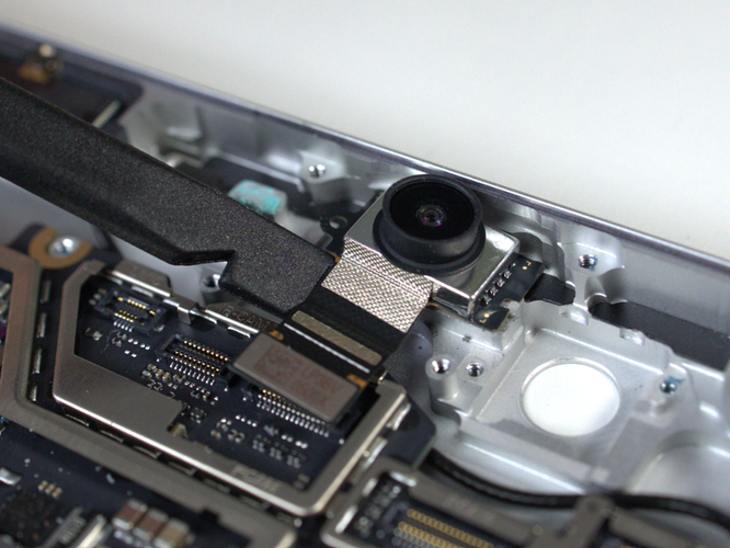 Screenshot that shows front camera being peeled up from enclosure with tool under right edge (re-use only).